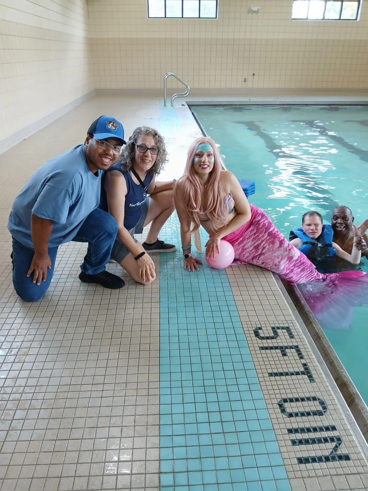 Residents and staff interacting with a mermaid by the pool
