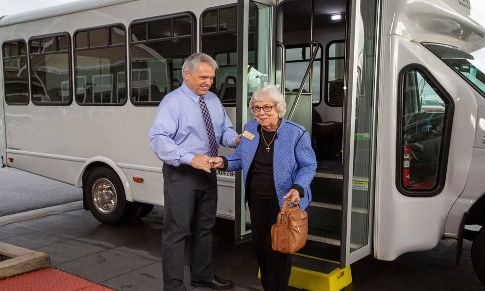 A staff member assists a resident exiting a shuttle bus.