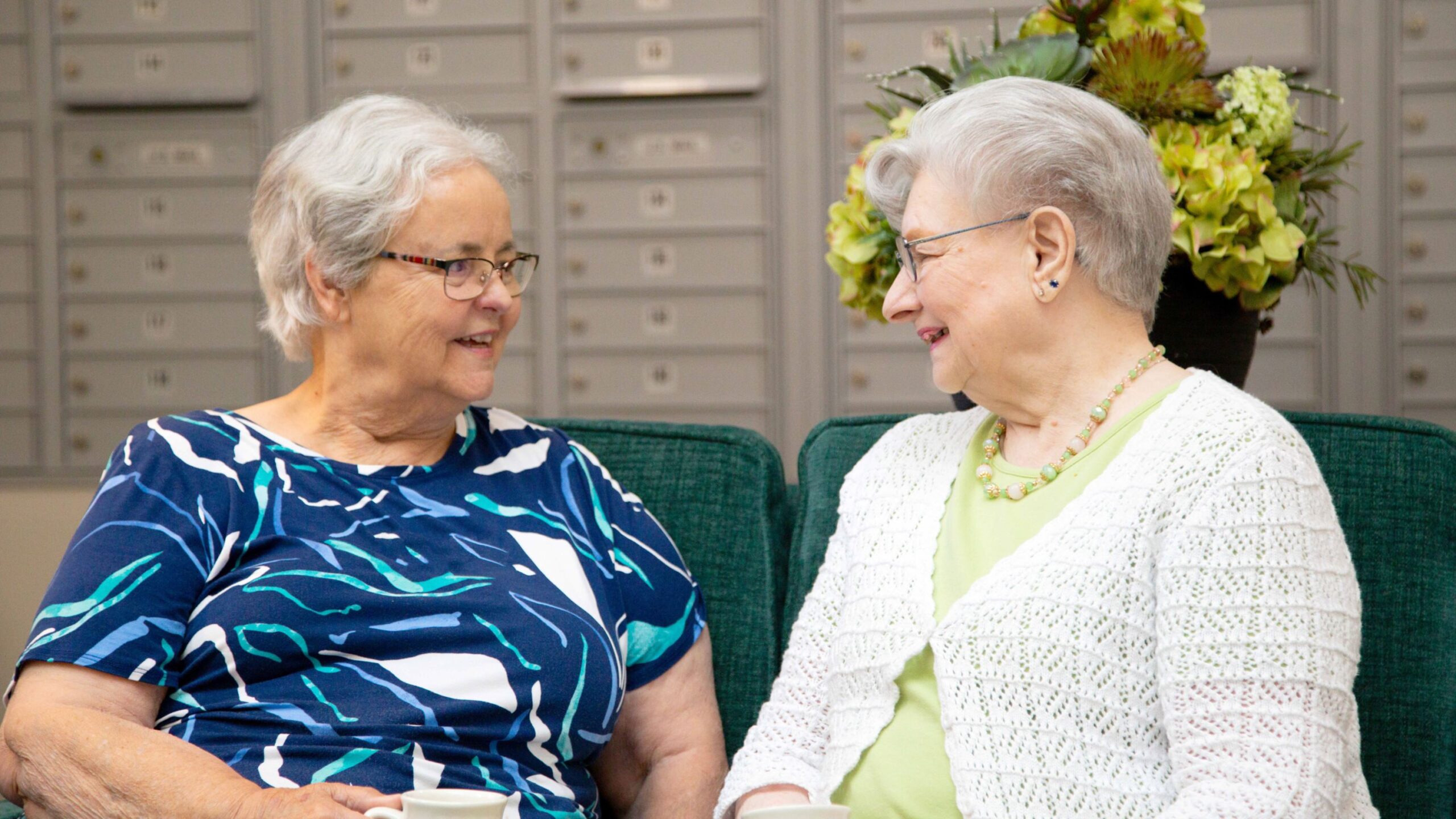 Two seniors engaged in conversation in a lounge area.