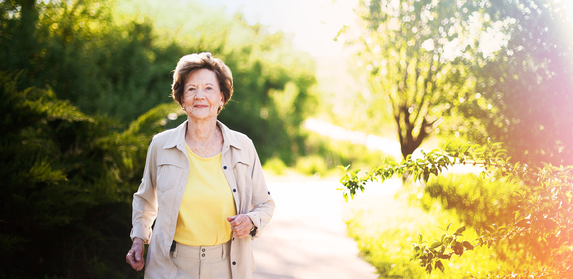 Elderly woman enjoying a walk in a lush, green area.