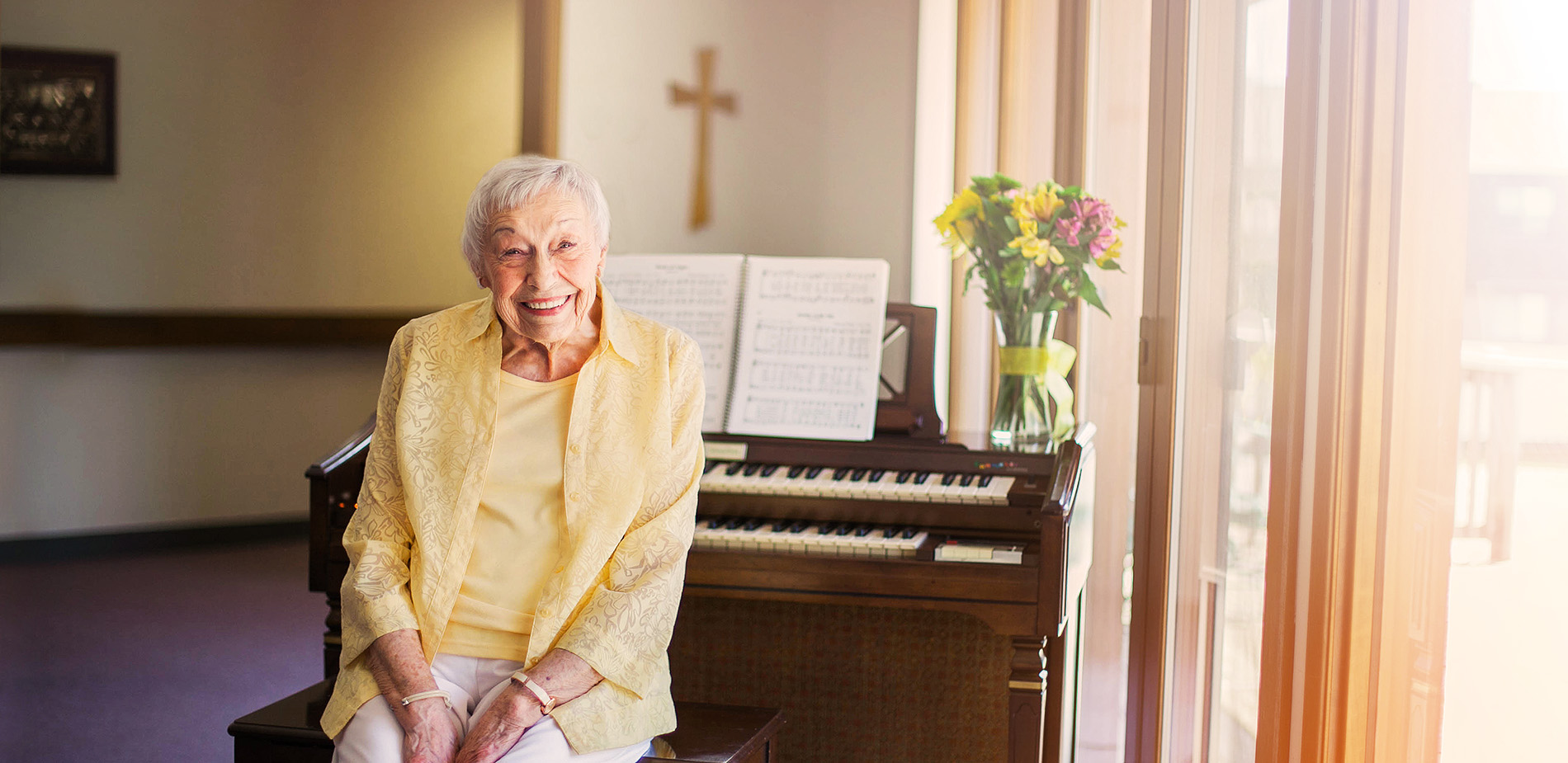 Elderly woman smiling at a piano with flowers
