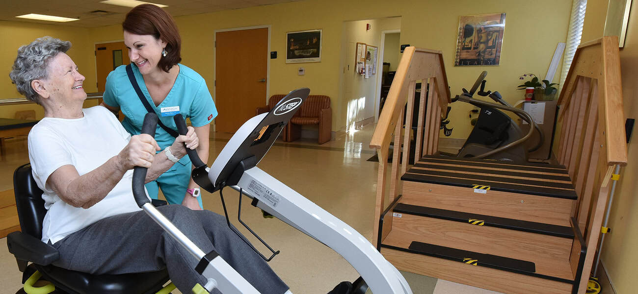 Staff assisting a resident with exercise equipment.
