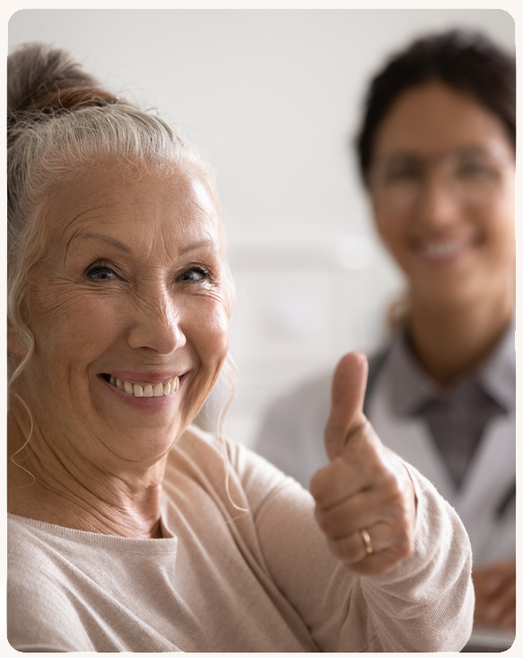 Happy elderly woman giving a thumbs up with staff in background.