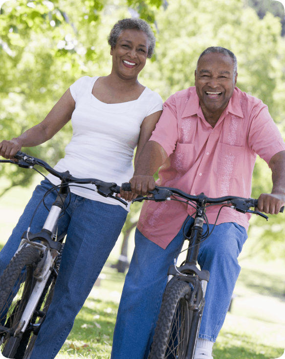 Two seniors smiling on bicycles in a park.