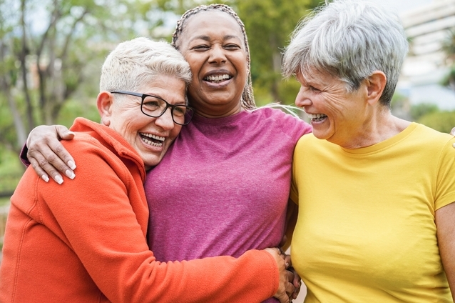 Three joyful women laughing together outdoors.