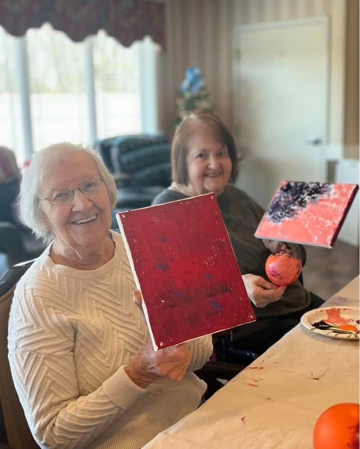 Two smiling seniors painting in a common area.