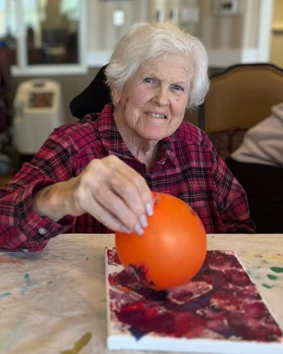 Senior resident painting with an orange balloon.