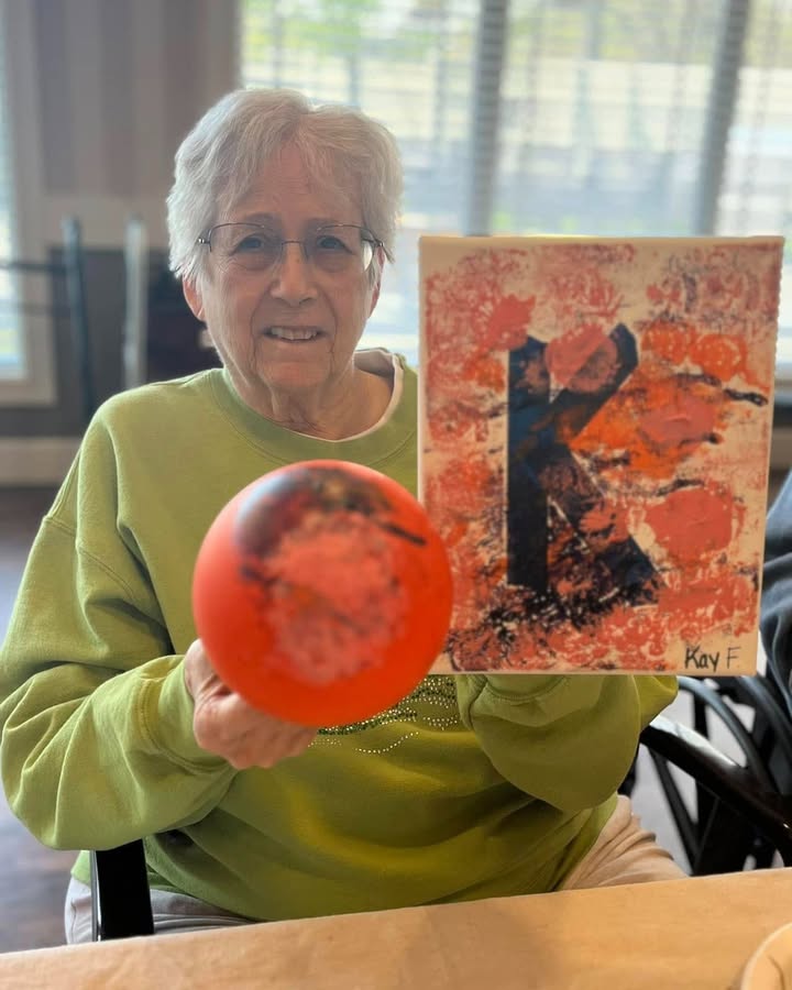Senior resident holding a painting and a ball.