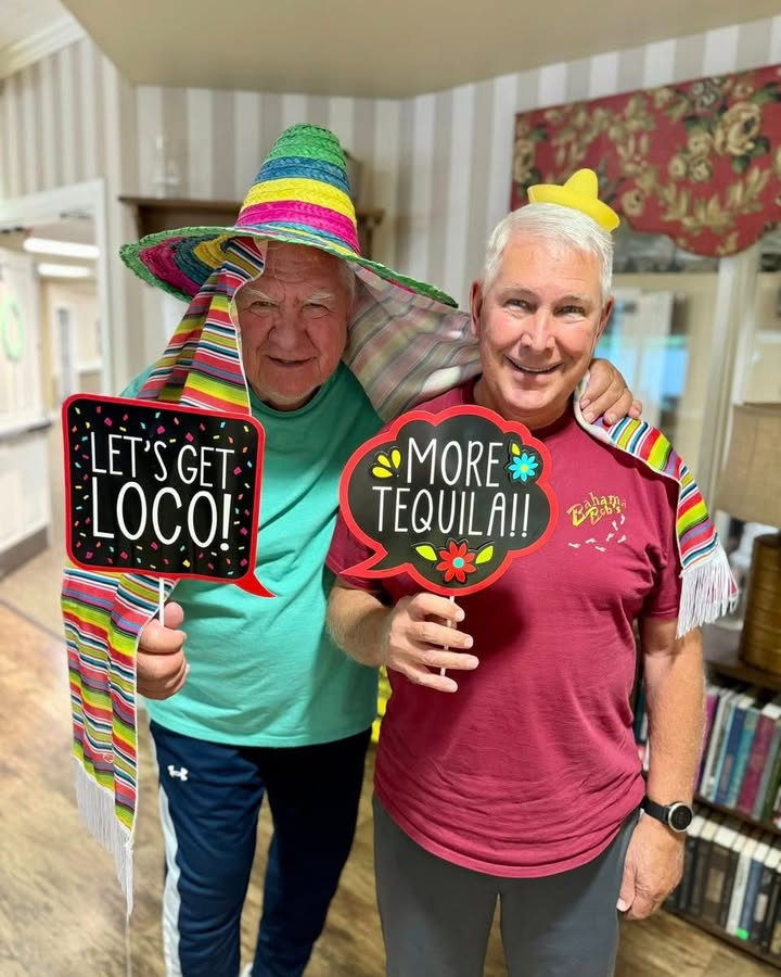 Two residents celebrating with playful signs indoors.