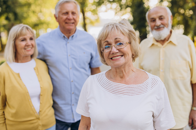 Four seniors smiling outdoors in a community setting.