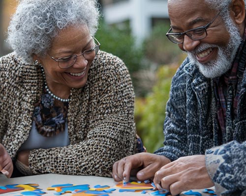 Two seniors working on a puzzle outdoors.