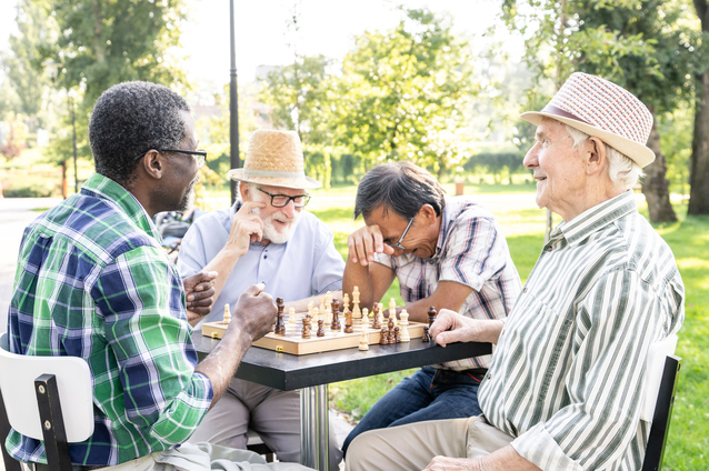 Seniors playing chess outside in a park.