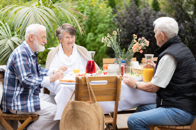 Seniors enjoying a meal outdoors in a garden setting.