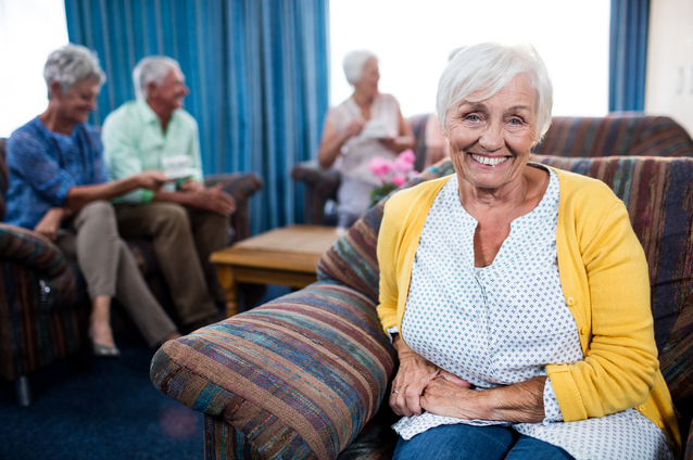 Smiling resident in a common area with others socializing.
