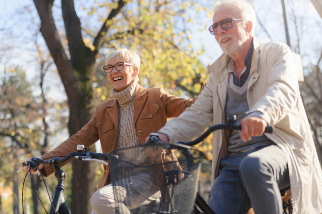 Two seniors riding bicycles outdoors.