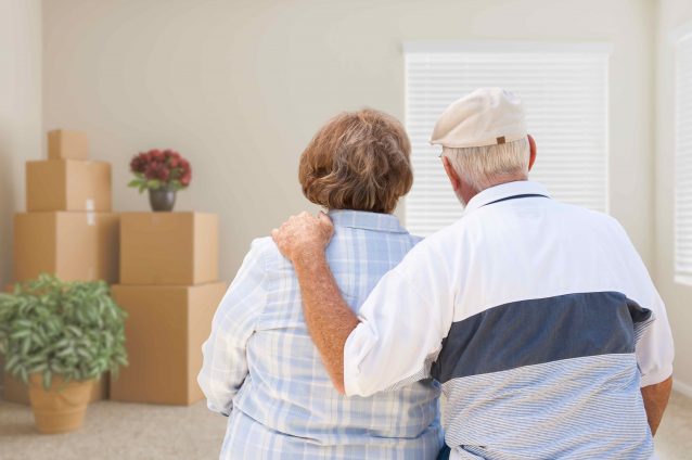 Couple embraces while surrounded by moving boxes.