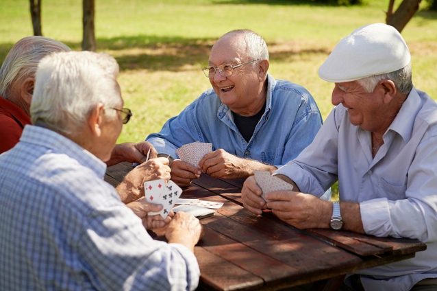 Seniors playing cards outdoors in a park setting.