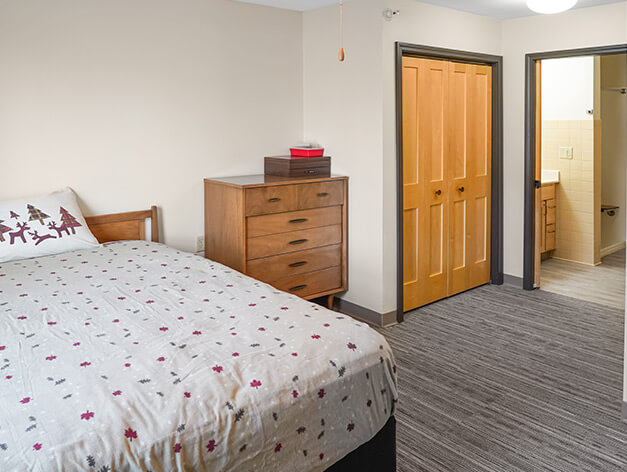 Brightly lit private resident room with a bed and dresser