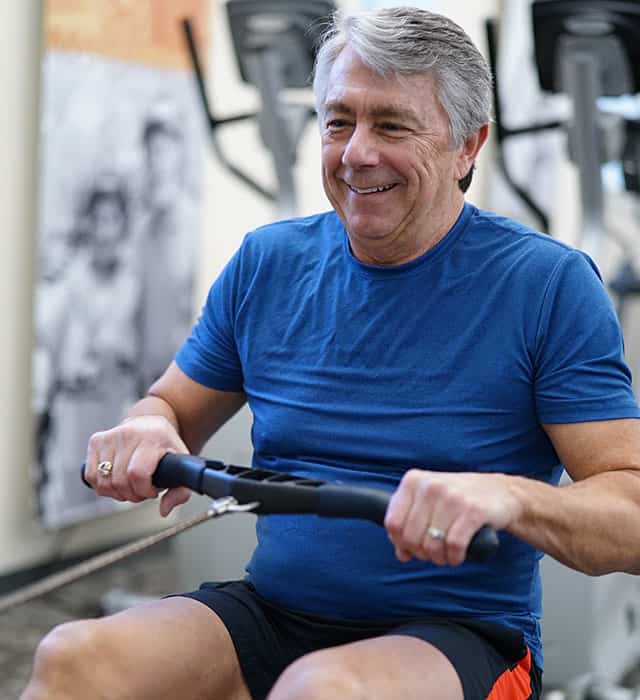 A senior man exercising on a rowing machine in a gym