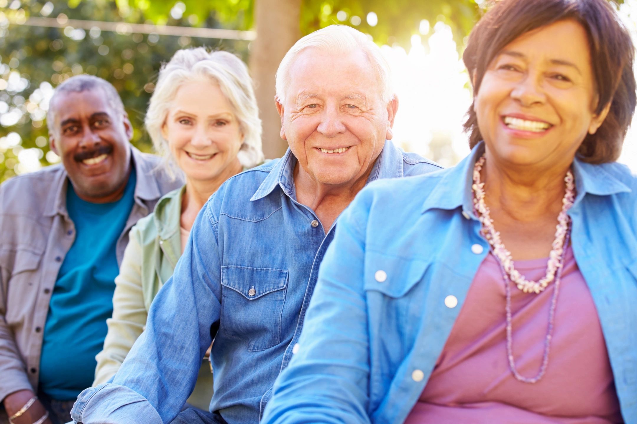Four seniors smiling outdoors in a sunny setting