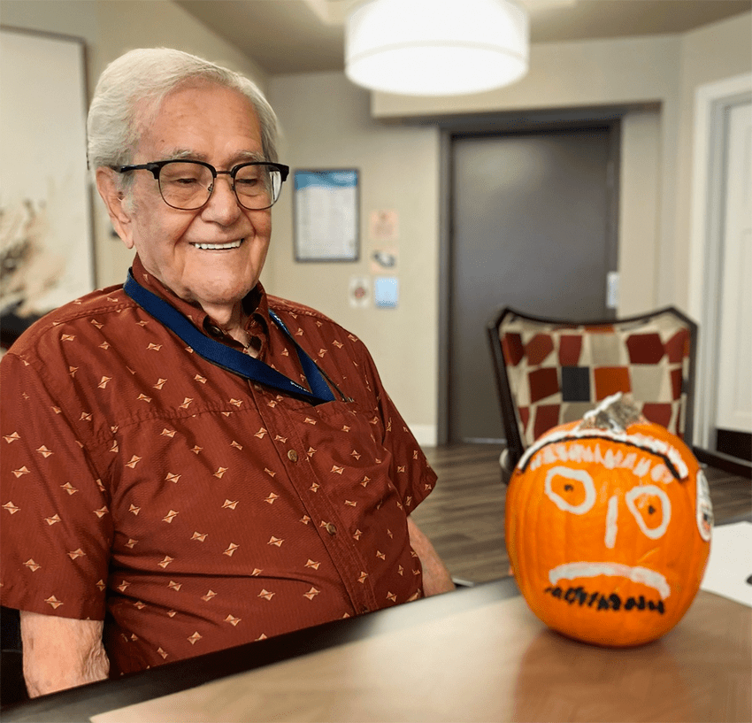 A resident smiling with a decorated pumpkin during an activity