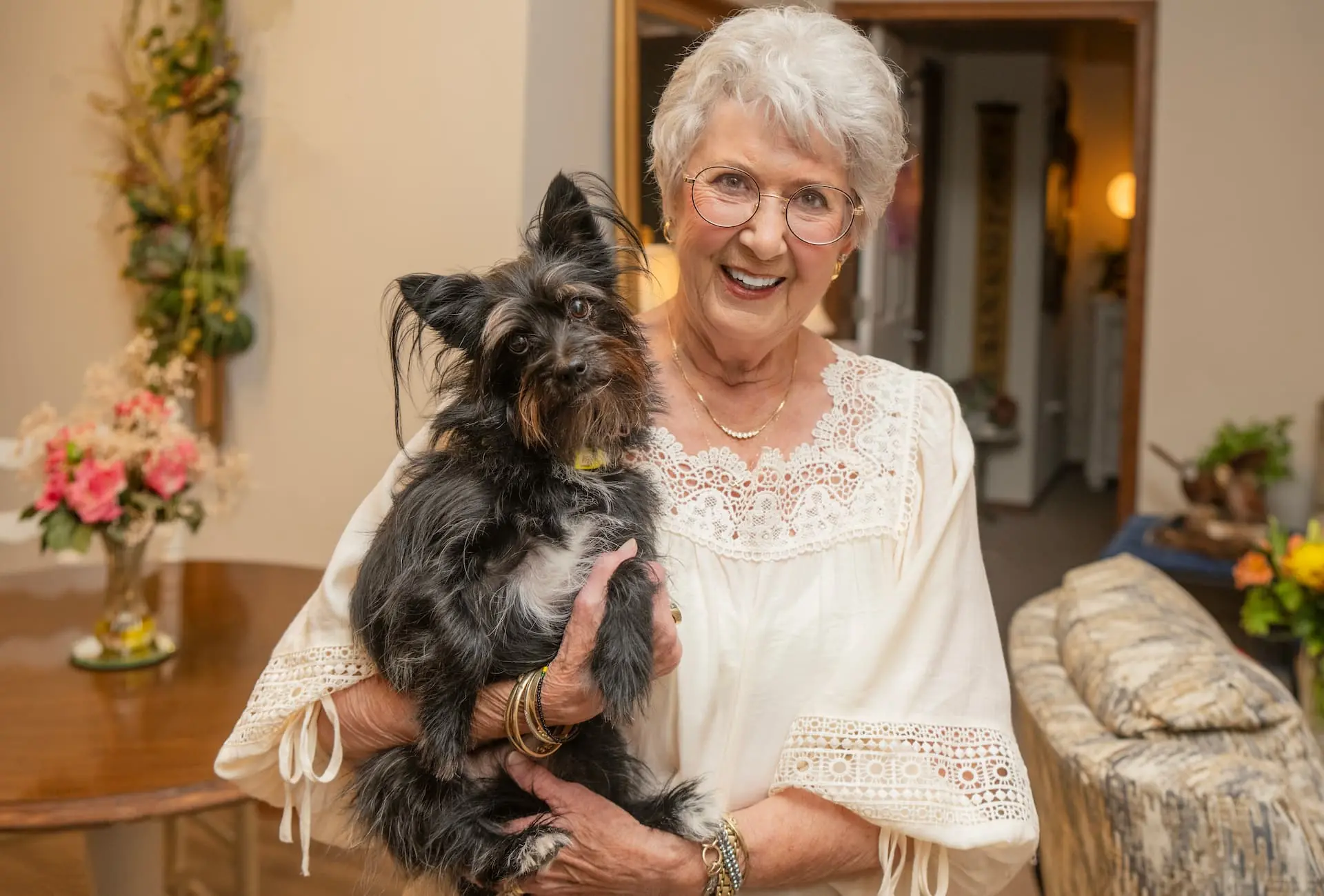 An elderly woman holding a small dog in a cozy living space