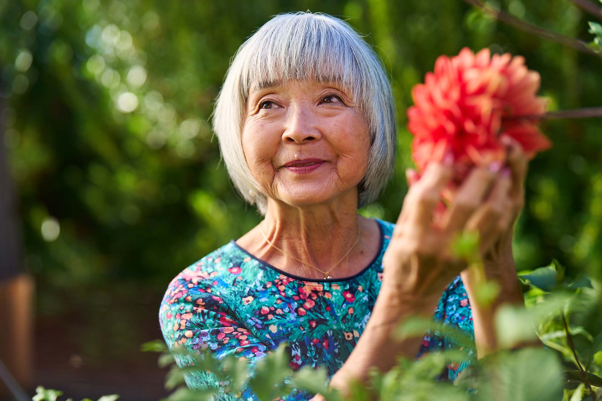 An elderly woman holding a flower in a garden