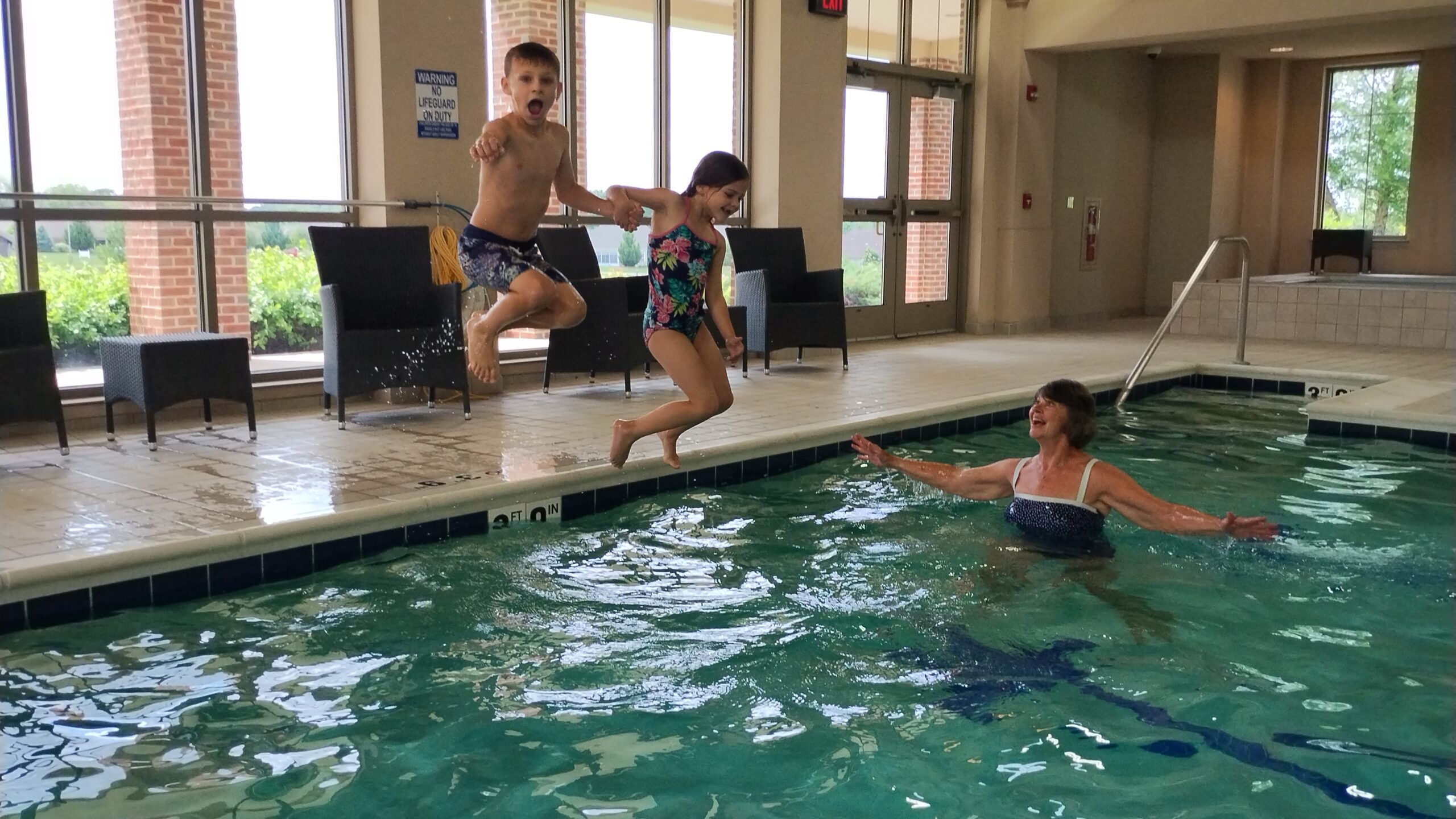 Children jumping into a swimming pool with an adult supervising