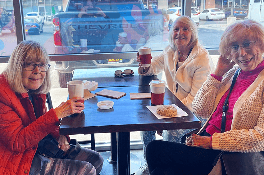 Three residents enjoying coffee at a common area table