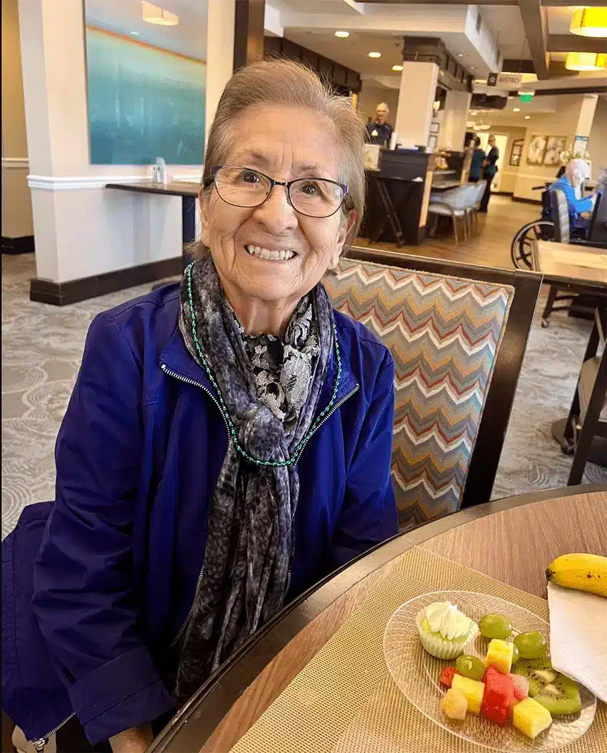 Resident smiling at a dining table with fruit