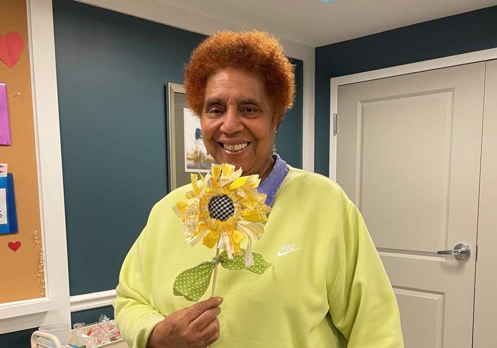 Resident holding a handmade sunflower craft in a common area