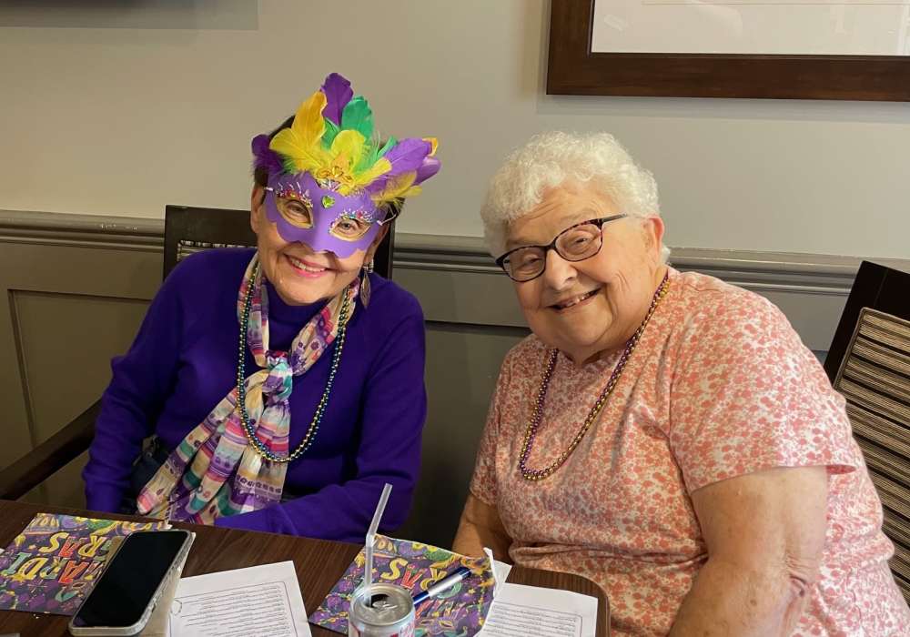 Two residents smiling with festive masks at a table