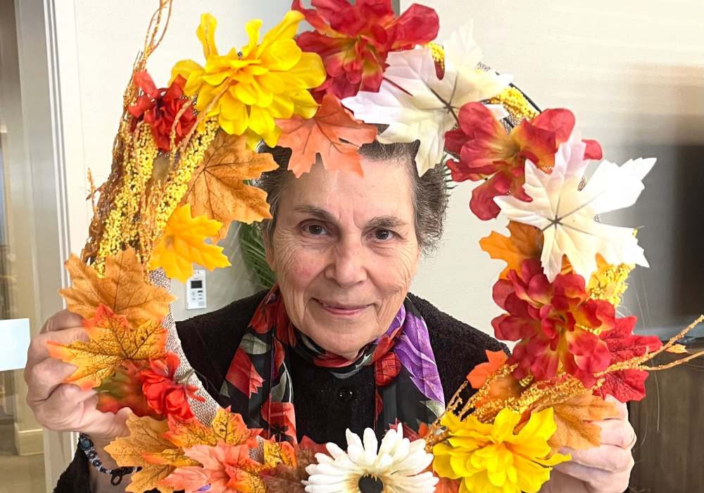 Resident showcasing a handmade fall wreath in an activity room