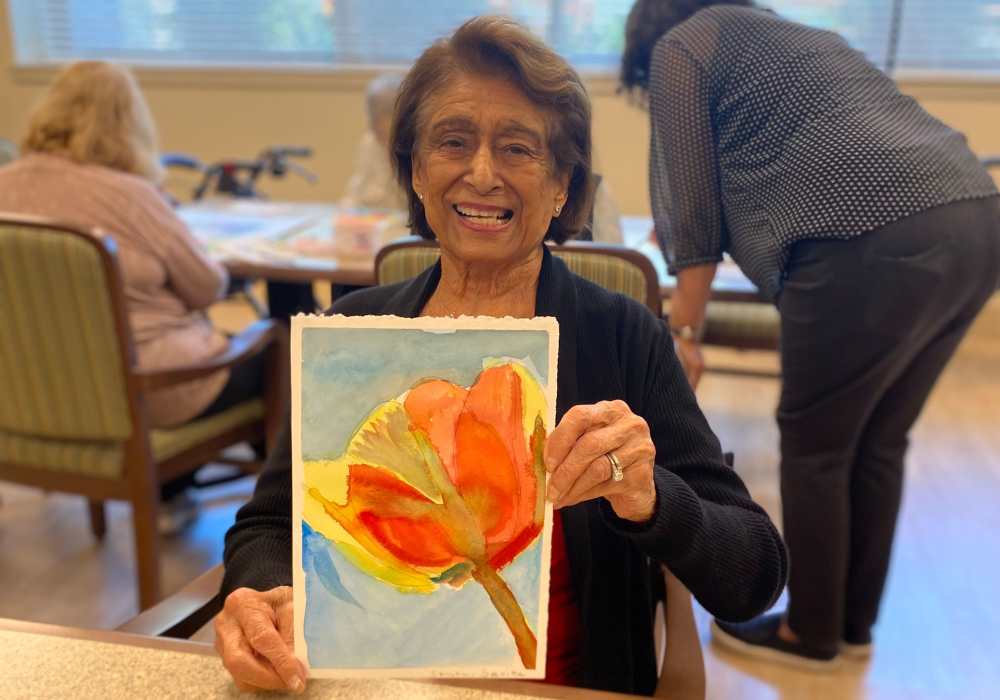 Resident holding a colorful watercolor painting in an activity room