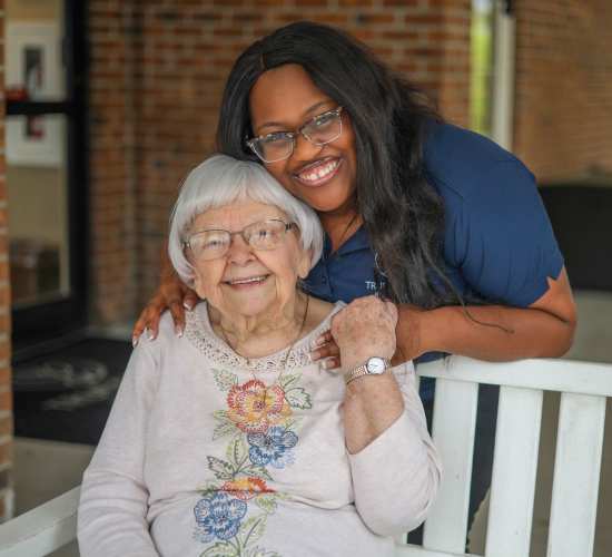 A senior resident smiling with a staff member outdoors