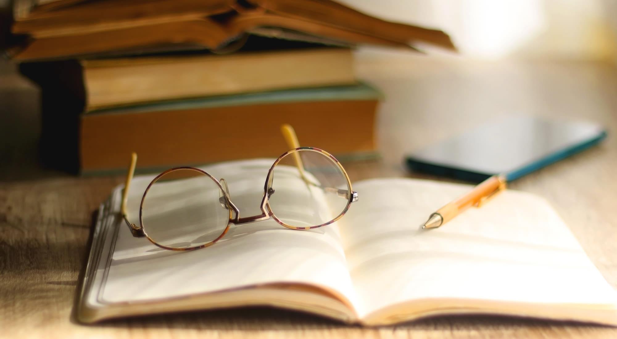 Reading glasses on an open book with a pen
