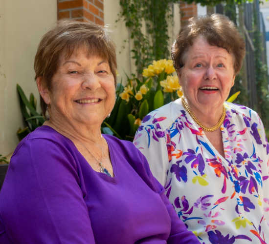 Two smiling women sitting in a garden area