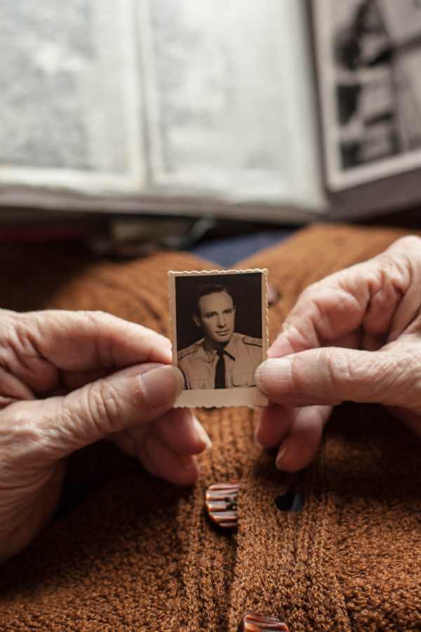Elderly hands holding a vintage photo of a man in uniform