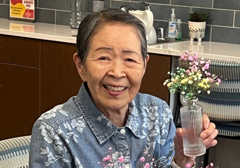 Senior resident smiling with flowers in a common area