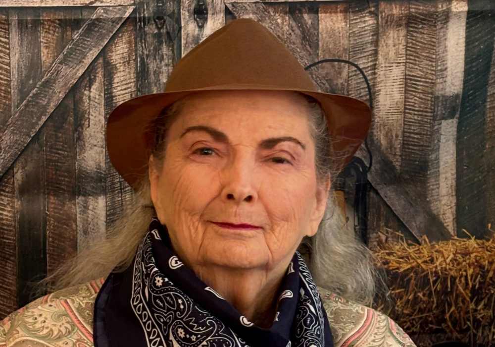 Elderly woman posing in a cowboy hat with a backdrop