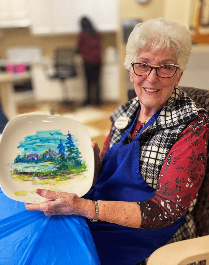 Resident proudly holds a painted plate in an activity room
