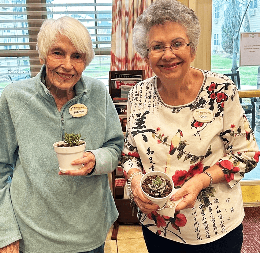 Two residents holding potted plants in a bright indoor space