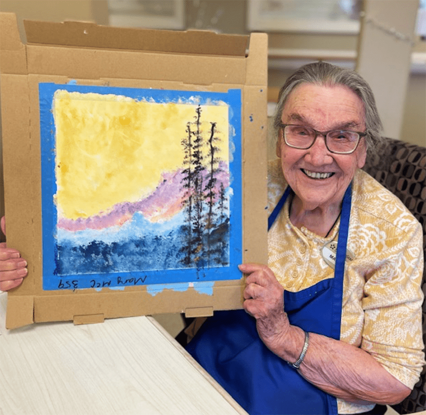 Resident showcasing her painting in an activity room