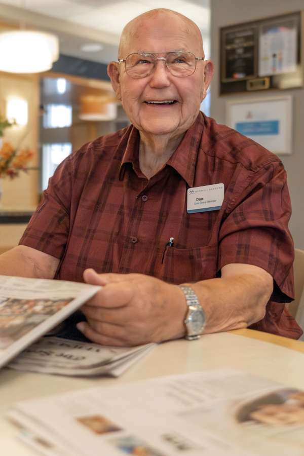 A resident smiling while reading a newspaper in a common area