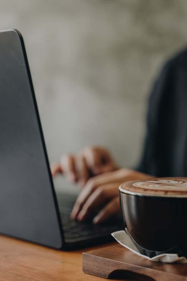 A person typing on a laptop with a coffee cup