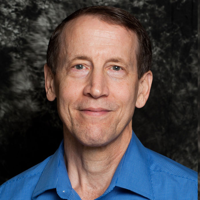 A smiling man in a blue shirt against a dark background
