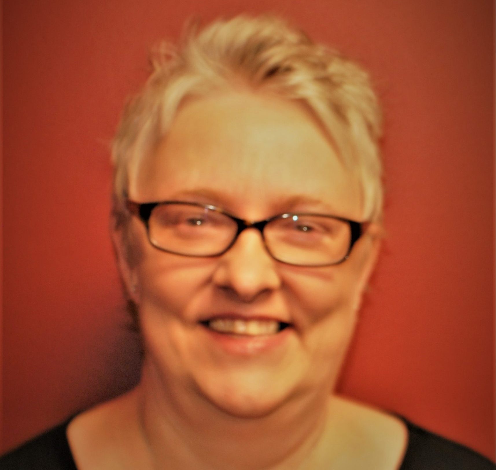 Smiling resident with glasses against a red wall