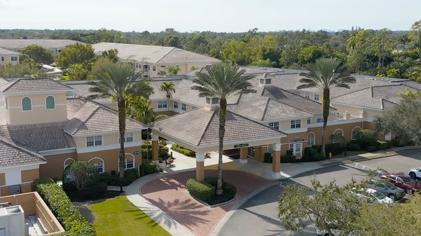 Aerial view of a senior living facility with gardens and palm trees