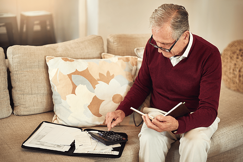 Senior man using a calculator and notepad in a cozy setting