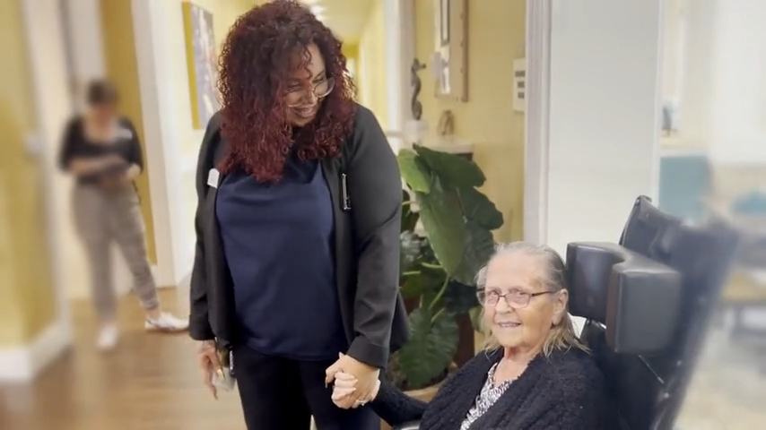 Staff member holding hands with a resident in a bright common area